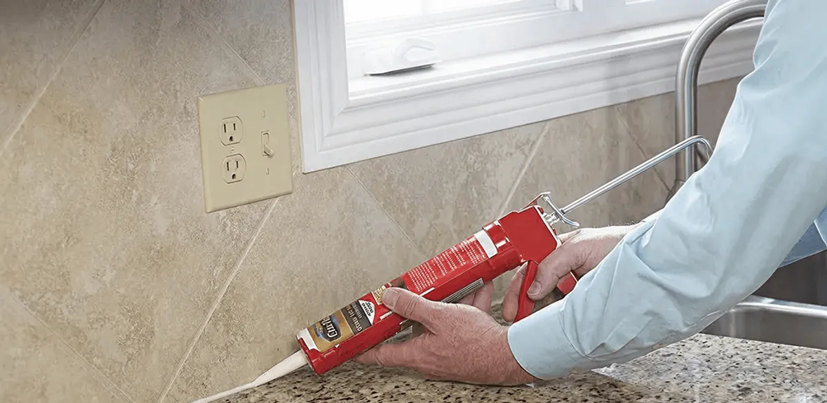 Handyman applying caulk along a kitchen backsplash and countertop seam in Akron, OH