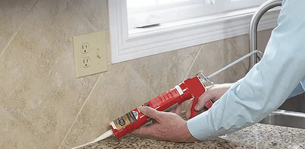 Handyman applying caulk along a kitchen backsplash and countertop seam in Akron, OH