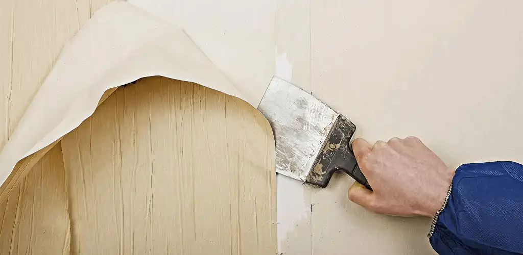 Handyman removing wallpaper with a scraper for wall preparation in Akron, OH